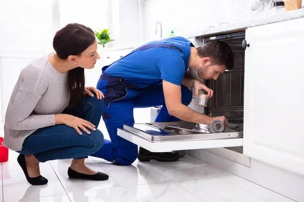 Technician checking a dishwasher while a homeowner watches