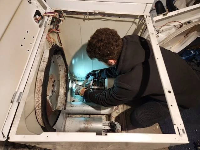 Technician inspecting the internal drum and mechanical components of an opened laundry appliance