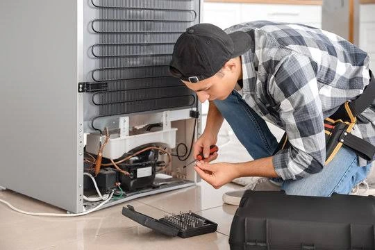 Technician checking the compressor and wiring at the back of a refrigerator