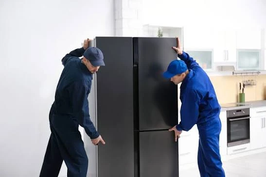 Two technicians positioning a black refrigerator in a kitchen